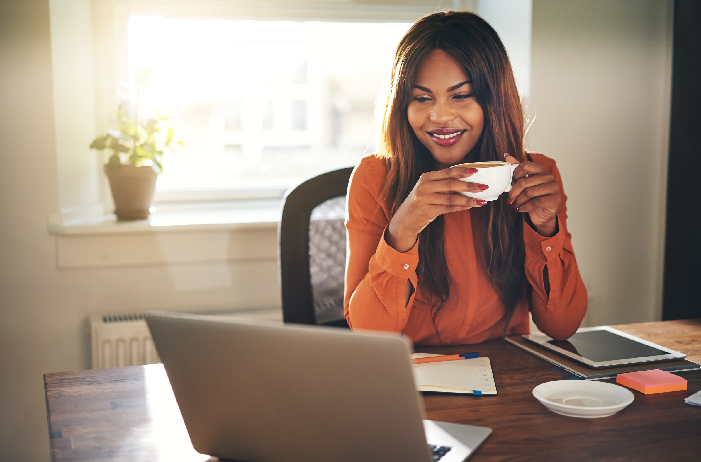 Smiling young woman drinking coffee while working from home